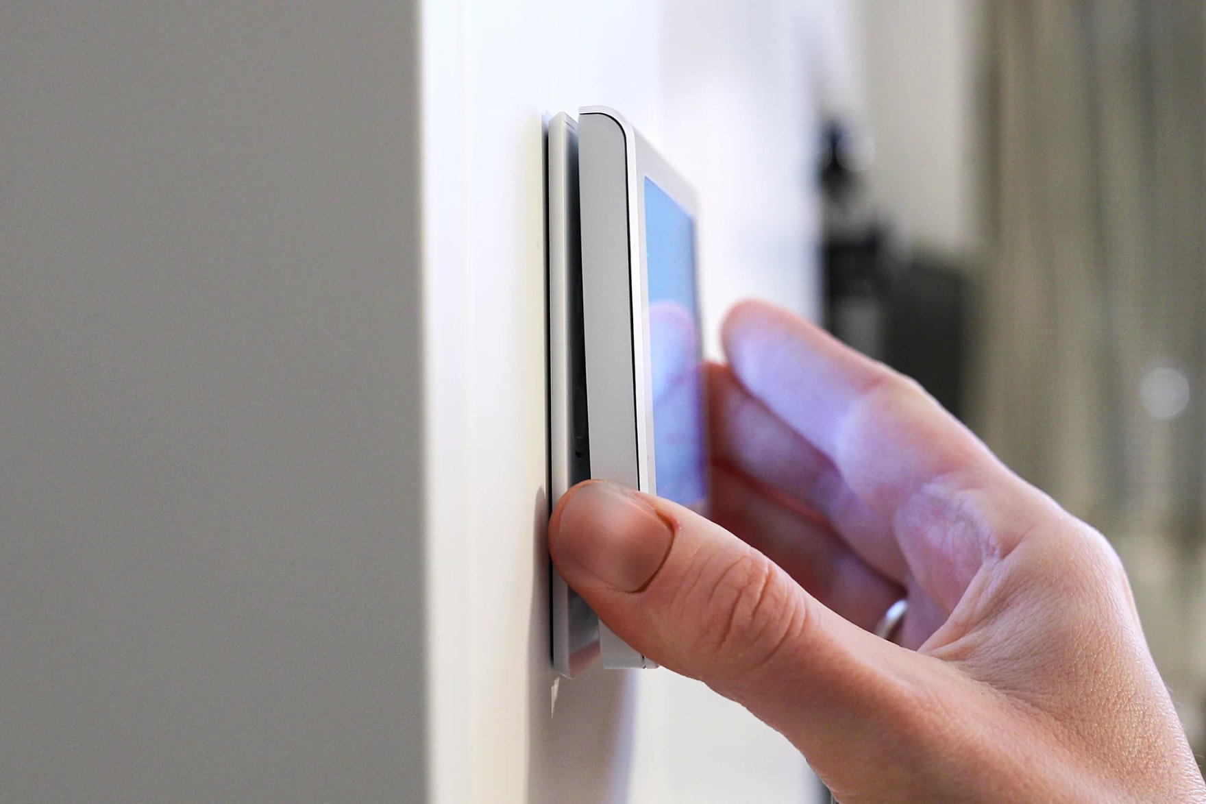 Une main décroche le thermostat RSQ800 de son support mural aimanté